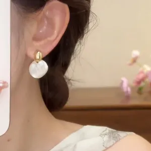 Primer plano de pendientes redondos minimalistas en oro y blanco puestos en la oreja