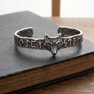 Nahaufnahme des Wikinger-Wolfskopf-Armreifs mit Runengravur auf einem alten Buch.