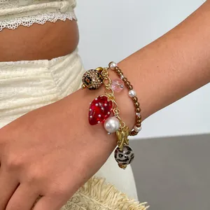 Detail van een meerlaagse bedelarmband met een aardbei van hars en witte parels.