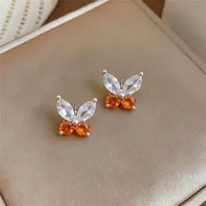 Detaillierte Nahaufnahme von eleganten Schmetterlingsohrsteckern mit orangefarbenen Zirkoniasteinen.