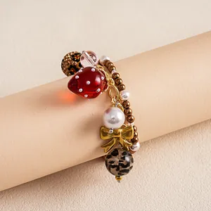Detailweergave van kralenarmband met rode hars aardbei, parels en luipaardbedeltjes.