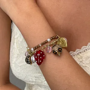 Gedetailleerd overzicht van een modieuze gelaagde armband met hart- en aardbeibedeltjes om een pols.