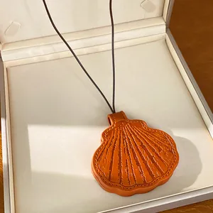Macro detail of a shell-shaped caramel leather pendant with fine artisan stitching