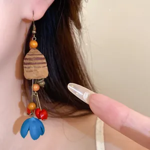Detailansicht von ethnischen Retro-Holzohrringen mit blauem Blumenanhänger am Ohr.
