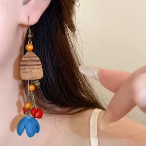 Detailaufnahme eines ethnischen Holz-Quastenohrrings mit blauer Blumenverzierung