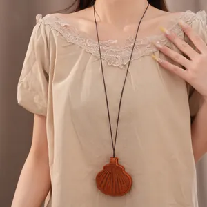 Detailed close-up of a brown leather shell-shaped glasses clip necklace worn on a beige dress.