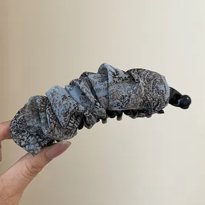 Gedetailleerde macro-weergave van de blauwe banaan-haarclip met retro luipaardprint plisséstof.