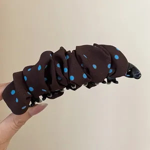 Gedetailleerd overzicht van een bruine geplooide bananenhaarklem met blauwe stippen