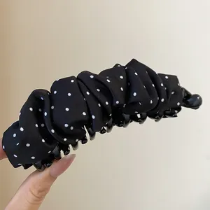 Detailweergave van een vintage zwarte bananenklem met witte stippen en plooistof