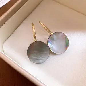 Elegante goldfarbene Hakenohrringe mit irisierenden runden dunklen Muschelanhängern in Geschenkbox