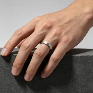 Minimalist brushed stainless steel ring worn on a male hand over stone background.