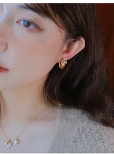 Close-up van een model met vintage goudkleurige pareloorbellen en een hartjesketting.
