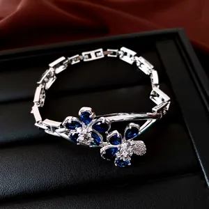 Primer plano de una pulsera de plata con flores de circón azul en un soporte negro.