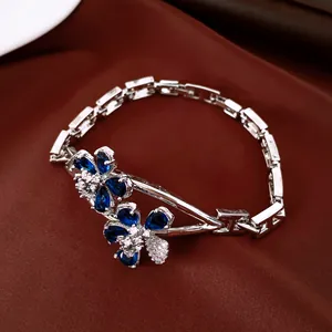 Primer plano detallado de una elegante pulsera de plata dorada con flores de circonita azul.