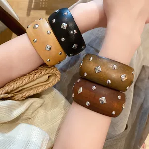 Detailansicht von gestapelten Retro-Armreifen mit silbernen rautenförmigen Nieten.