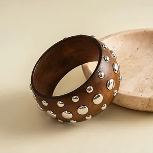 Detailansicht der Holzmaserung und glänzenden Metallnieten dieses Retro-Resin-Armreifs