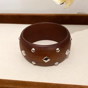 Nahaufnahme eines Retro-Armreifs aus dunklem Holz mit geometrischen silbernen Nieten.