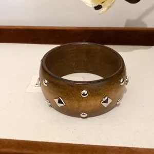 Nahaufnahme eines Vintage-Holzarmbandes mit runden und rautenförmigen Metallnieten.