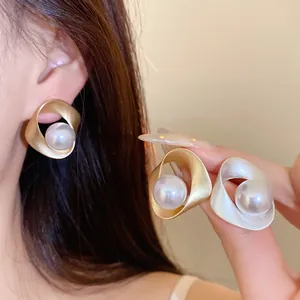 Detailweergave van geometrische matgouden en zilveren oorbellen met ronde parels op model.