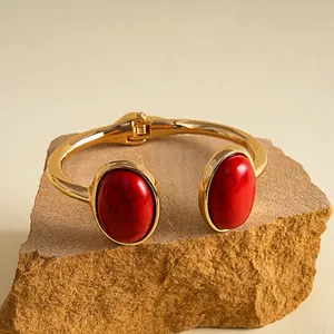 Nahaufnahme eines goldenen Armreifs im Retro-Stil mit ovalen roten Kunstharzsteinen.