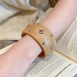 Nahaufnahme eines Vintage-Armreifs mit Holzmaserung und silbernen Nieten auf dem Arm.