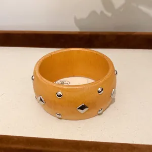 Nahaufnahme eines Vintage-Holzarmreifens mit geometrischen silbernen Metallnieten