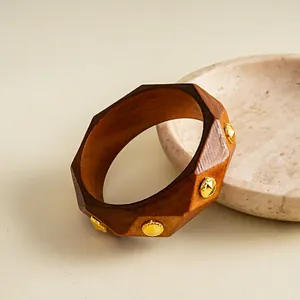 Makroansicht eines Retro-Harz-Armreifs mit Holzmaserung und goldfarbenen Metallnieten.