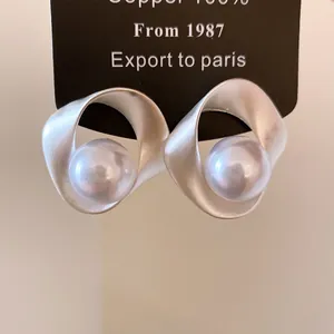 Detailopname van geometrische zilverkleurige oorbellen met grote witte glanzende parels.
