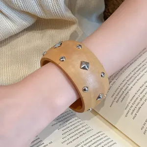 Nahaufnahme eines Retro-Holzarmreifens mit geometrischen Silbernieten am Handgelenk