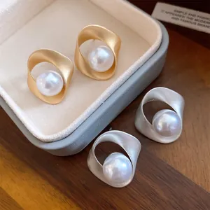 Detailweergave van mat gouden en zilveren geometrische oorbellen met witte parels