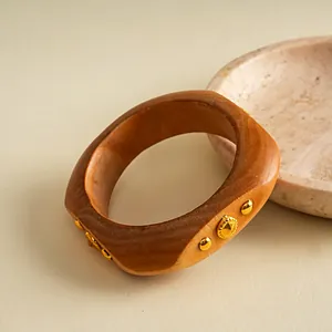 Nahaufnahme eines Retro-Harz-Armreifs mit goldenen Metallnieten und Holzmaserung