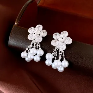 Close-up detail of silver floral stud earrings with cascading pearl tassels and zircons