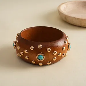 Eine Detailaufnahme eines Retro-Holzarmreifens mit Goldnieten und Türkis-Einlagen.
