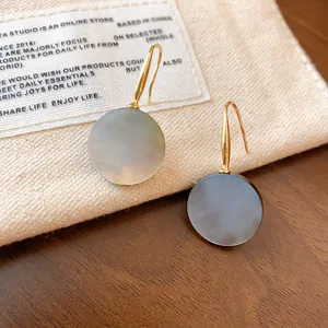 Detailansicht der geometrischen runden Muschel-Ohrhänger mit goldenen Haken auf Stoff