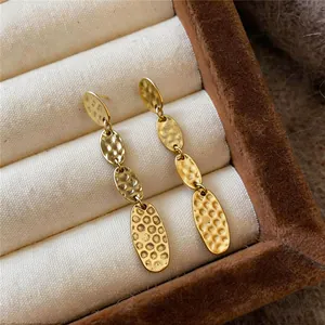 Detalle de pendientes colgantes ovalados de metal martillado dorado con textura.