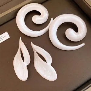 Elegante witte emaille spiraal en abstracte blad oorbellen op bruine tray