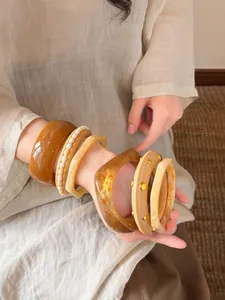 Nahaufnahme von geometrischen Harzarmreifen und Perlenarmbändern am Handgelenk.