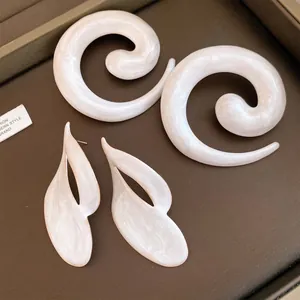 Detail van parelwitte emaille oorbellen in spiraalvorm en abstracte bladvorm, stijlvol.