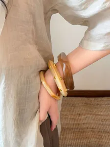 Detailansicht eines Modells, das drei Harzarmbänder in Bernstein und Beige trägt.