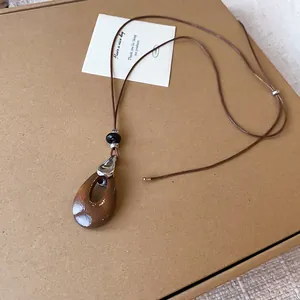 Vue détaillée d'un collier avec pendentif goutte d'eau, cordon marron et accents métalliques