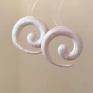 Detail van minimalistische spiraalvormige oorbellen met parelmoer marmeren druppelolie textuur