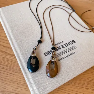 Gros plan de colliers à pendentif goutte d'eau minimalistes en noir et marron.