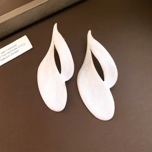 Close-up van elegante witte emaille druppelende olie gedraaide vlamvormige oorknopjes