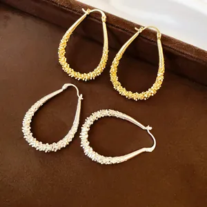 Close-up view of elegant gold and silver water-drop hoop earrings with a textured finish.