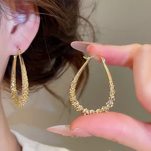 Close-up view of elegant geometric teardrop hoop earrings featuring a gold textured finish