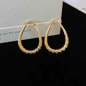 Close-up of gold finish geometric waterdrop hoop earrings with intricate textured details.