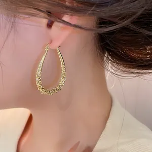 Close-up view of elegant gold waterdrop hoop earrings with textured finish worn by model