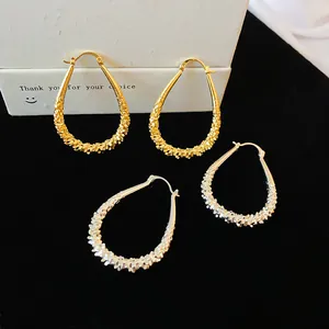 Close-up of geometric teardrop hoop earrings with textured metallic finish
