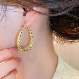 Close-up of elegant gold teardrop hoop earrings with a unique grainy textured finish