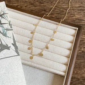 Détail d'un collier chaîne doré délicat avec de nombreuses petites médailles rondes suspendues